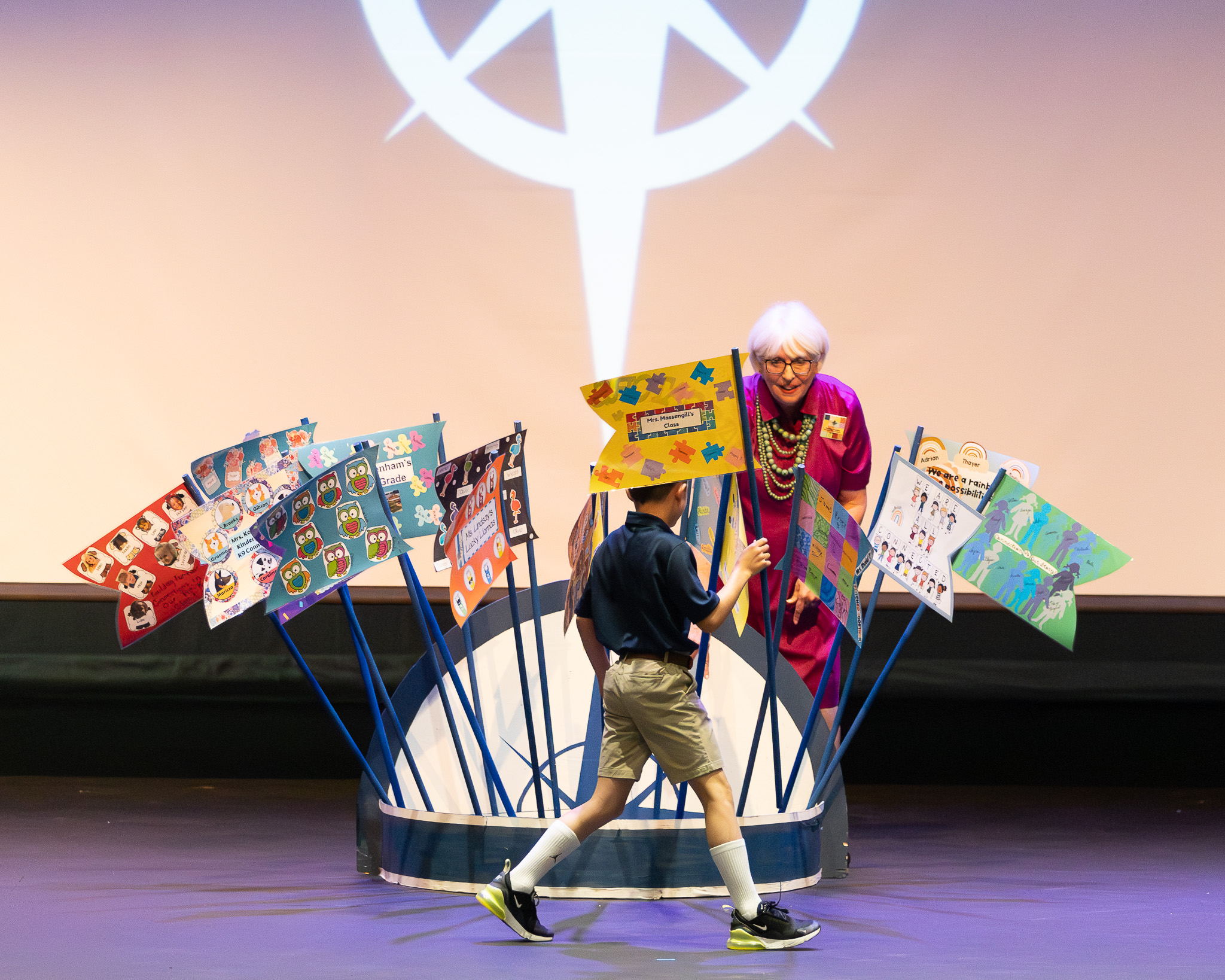 HRA Director of Lower School Susanne Swain '78 welcomes class flag bearers to the stage at the first Lower School Leadership Assembly of the 2025-2026 school year